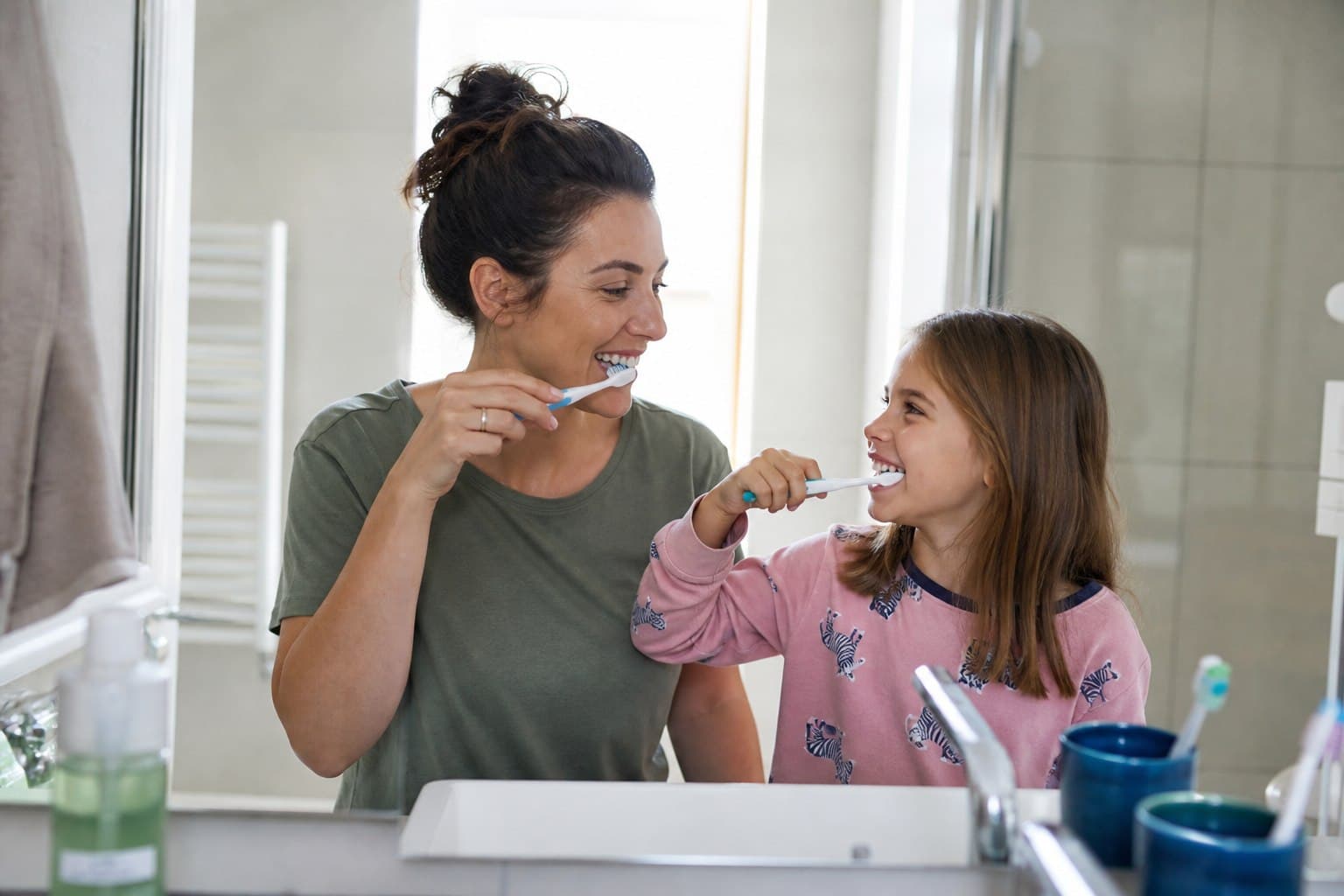 A parent and child brushing their teeth at a home bathroom sink